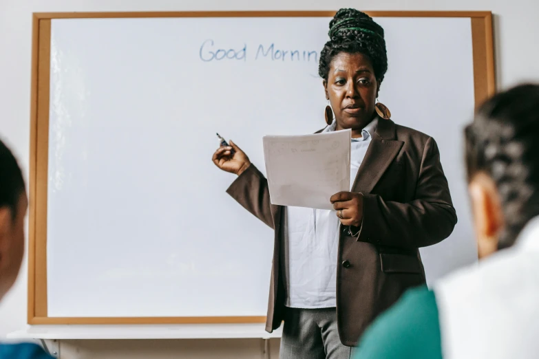 a woman standing in front of a whiteboard holding a piece of paper, pexels contest winner, ashcan school, teaching, te pae, background image, early in the morning