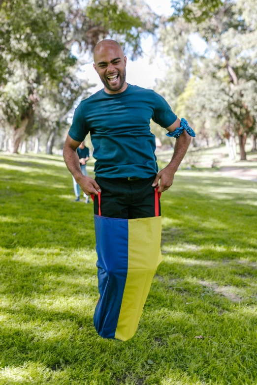 a man standing on top of a lush green field, in blue and yellow clothes, large pants, mutahar laughing, wearing fitness gear