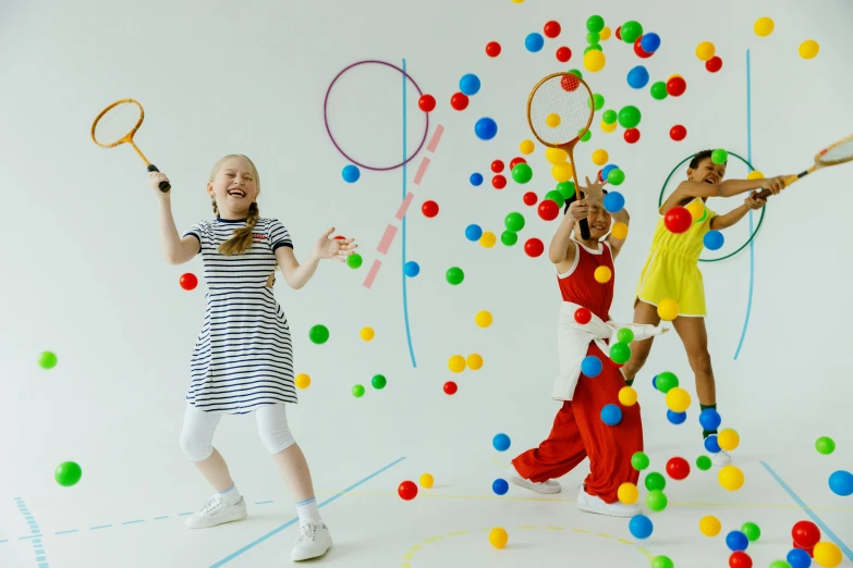 a couple of girls standing next to each other holding tennis racquets, by Julia Pishtar, interactive art, many floating spheres, primary colours, families playing, studio shoot