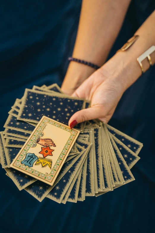 a woman holding a deck of playing cards, by Julia Pishtar, gold and indigo, charts, cottagecore hippie, high quality picture