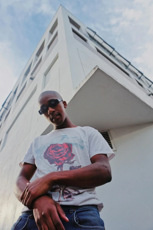 a man standing in front of a white building, an album cover, inspired by Barthélemy Menn, unsplash, tupac, photo of a rose, wearing a t-shirt, florida man