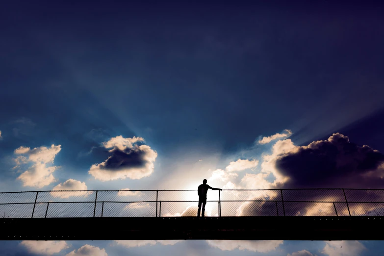 a silhouette of a person standing on a bridge, inspired by Storm Thorgerson, pexels contest winner, light and clouds, evening sunlight, contemplation, dramatic light 8 k
