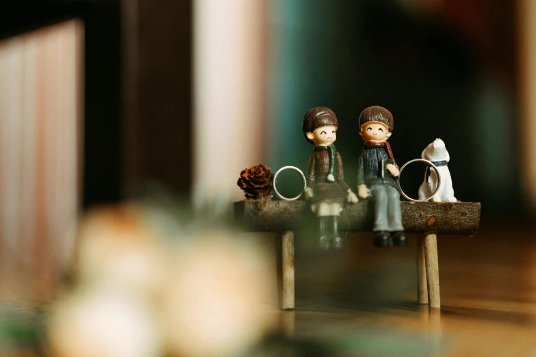 a couple of figurines sitting on top of a wooden bench, a tilt shift photo, by Emma Andijewska, pexels contest winner, folk art, cozy cafe background, cute boys, holiday season, high quality product image”