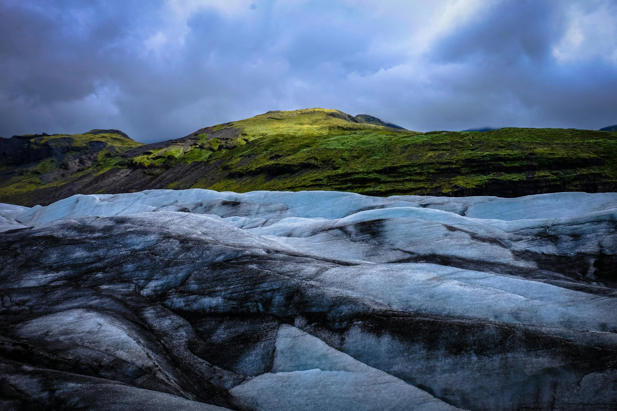 a mountain covered in green grass under a cloudy sky, unsplash contest winner, hurufiyya, covered in ice, blue sand, tessellated planes of rock, light and dark