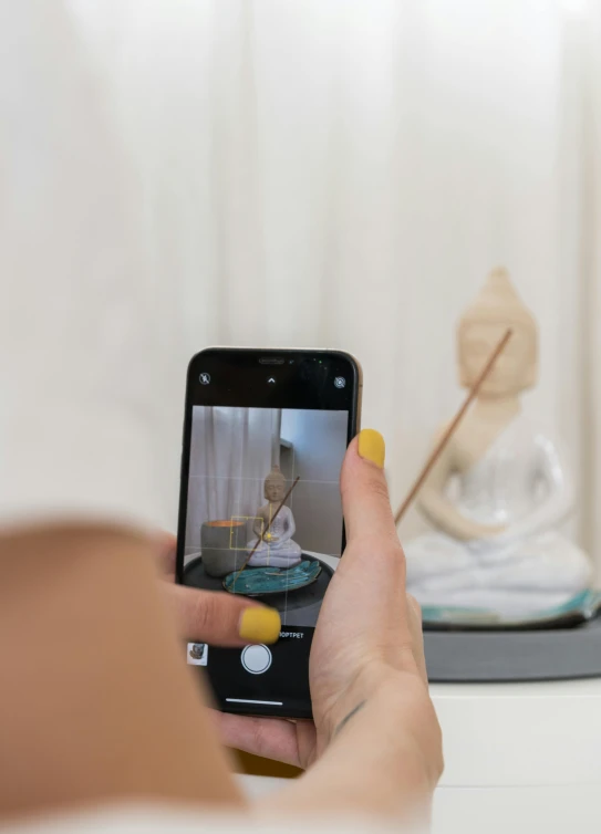 a close up of a person holding a cell phone, a picture, inspired by Li Di, unsplash, visual art, health spa and meditation center, tiny statue on display, instagram photo shoot, buddhist