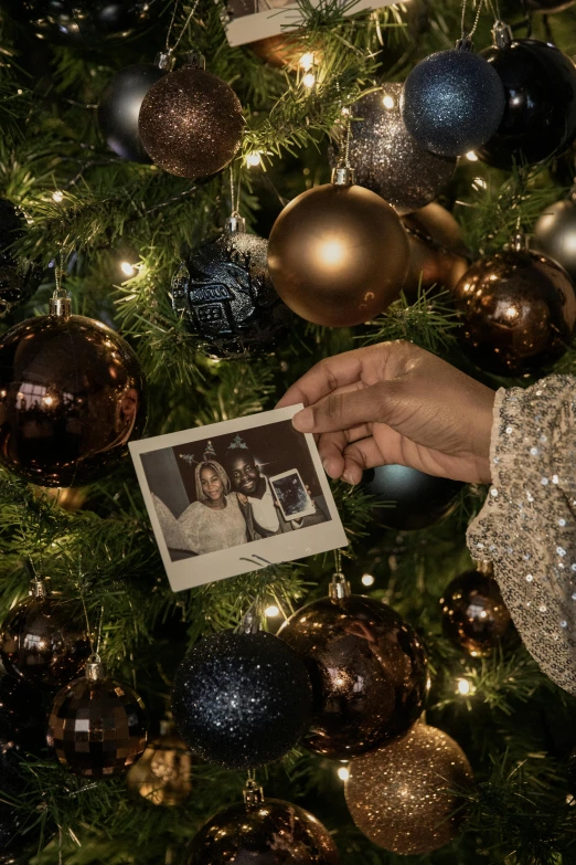 a person holding an old photo in front of a christmas tree, a polaroid photo, intricate ornament halo, had, f/9