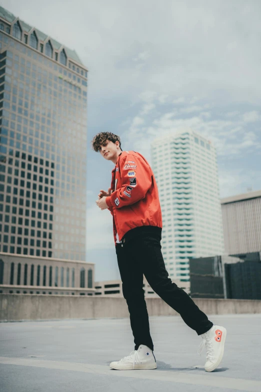 a man standing on top of a roof looking at his cell phone, an album cover, inspired by John Luke, wearing red jacket, tall buildings in background, official music video, profile photo