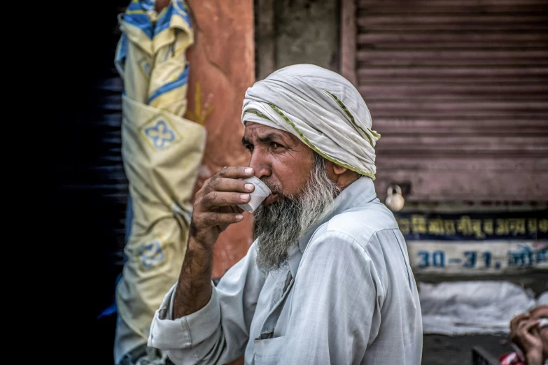 a man in a turban smokes a cigarette, inspired by Steve McCurry, pexels contest winner, with a white mug, drinking cough syrup, people watching around, indian