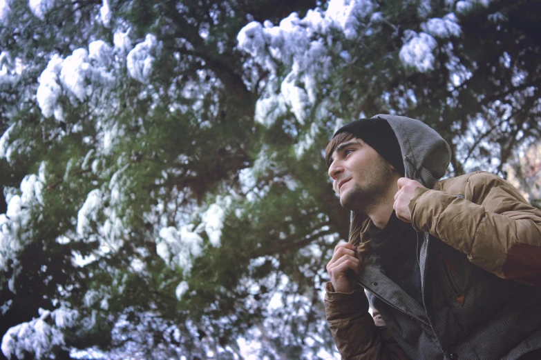 a man with a backpack standing in front of a tree, a picture, by Lucia Peka, unsplash, conceptual art, dusting of snow, still from a music video, looking up at camera, in avila pinewood