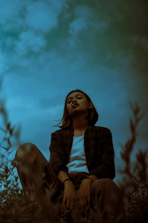 a woman sitting on top of a grass covered field, inspired by Elsa Bleda, pexels contest winner, aestheticism, smoking, (night), under blue clouds, androgynous person