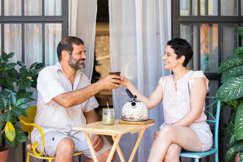 a man and a woman sitting at a table eating cake, greek ameera al taweel, holding a drink, avatar image, natural light outside