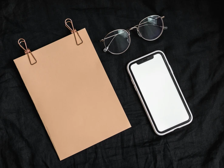 a cell phone sitting on top of a piece of paper next to a pair of glasses, cell cover style, with a black background, holding a clipboard, flatlay