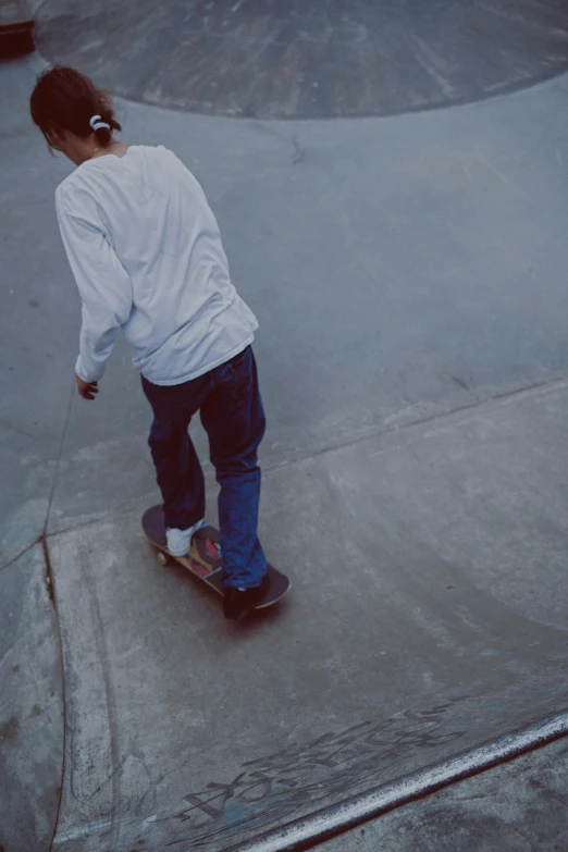 a person riding a skateboard at a skate park, by Pablo Rey, trending on unsplash, grainy film still, white shirt and blue jeans, walking away, top - down