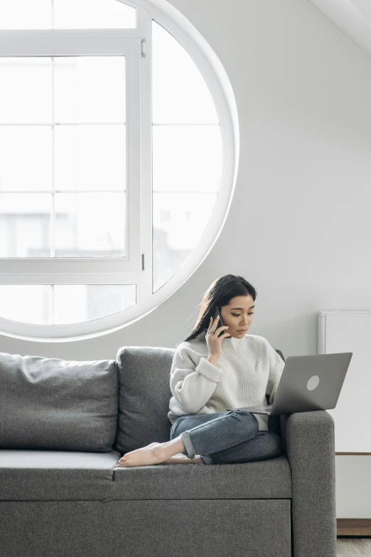 a woman sitting on a couch using a laptop, pexels contest winner, minimalism, girl making a phone call, white and grey, inspect in inventory image, asian woman