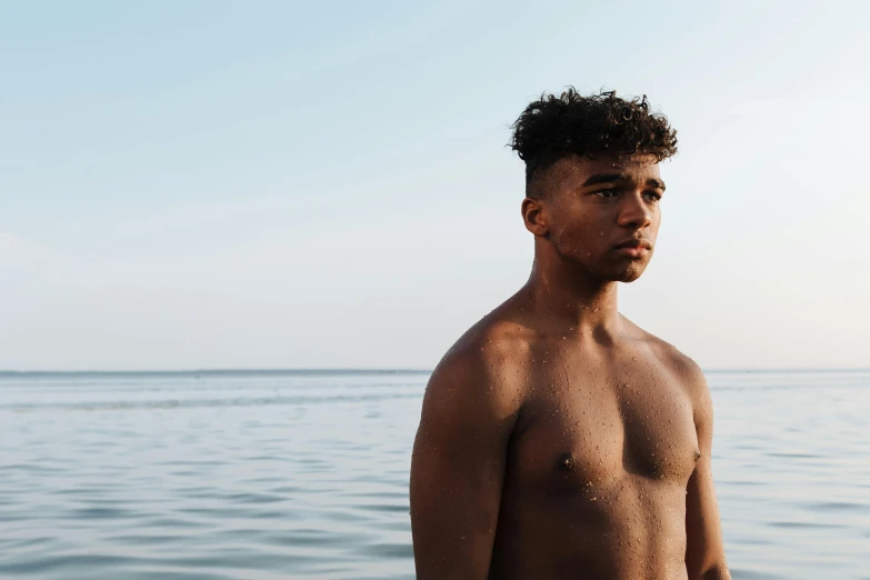 a man that is standing in the water, by Carey Morris, pexels contest winner, light brown skin, he is about 20 years old | short, curls on top, sea in the background