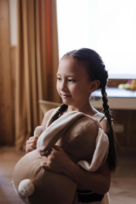 a little girl holding a stuffed animal in her arms, a portrait, by Adam Marczyński, pexels contest winner, wearing a towel, long braided hair pulled back, holding a gold bag, at home