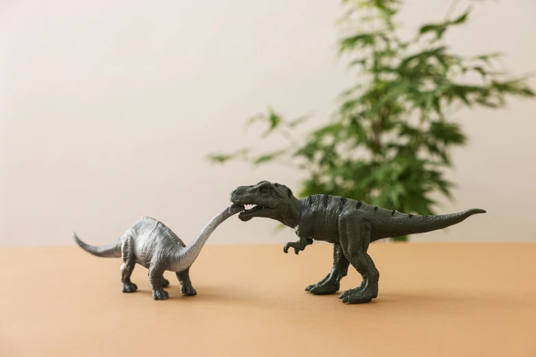 a couple of toy dinosaurs standing next to each other, inspired by Adam Rex, trending on unsplash, new sculpture, grey, next to a plant, devouring a planet, serpentine pose