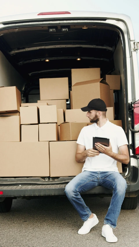 a man sitting in the back of a van holding a tablet, box, trucks, feature, square