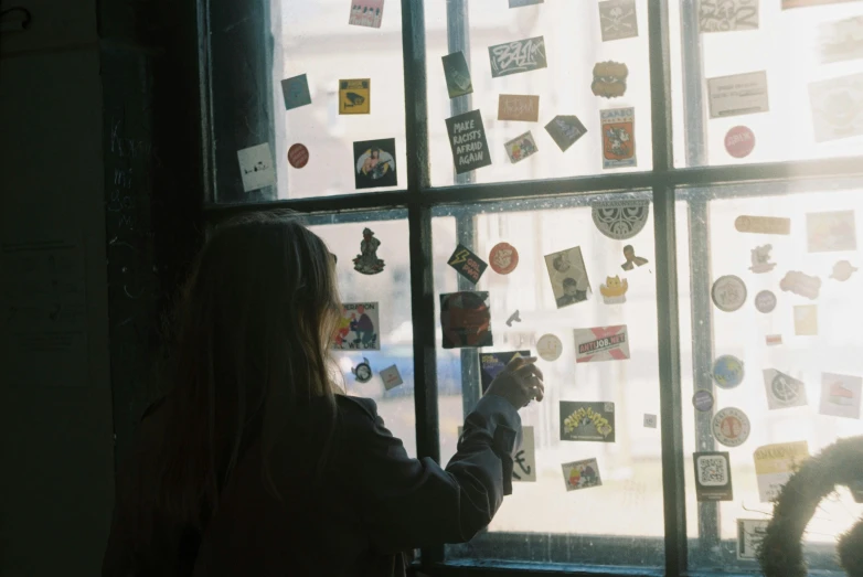 a woman standing in front of a window covered in magnets, a polaroid photo, inspired by Elsa Bleda, pexels contest winner, visual art, unused sticker sheet, in a coffee shop, labels, facing away