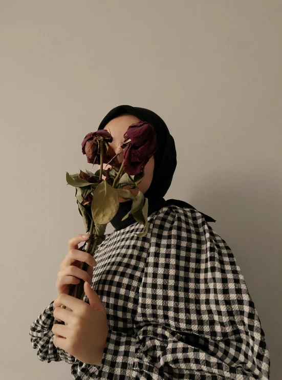 a woman holding a flower in front of her face, inspired by irakli nadar, unsplash, aestheticism, chequered cape, hijab, aesthetic ”
