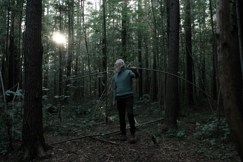 a man standing in the middle of a forest, holding a bow, lynn skordal, documentary still, evening lighting