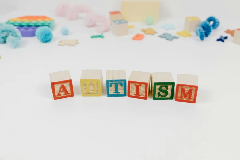 wooden blocks spelling autism on a white surface, by Ruth Simpson, letterism, full body photograph, petite, 3 d print, wood print