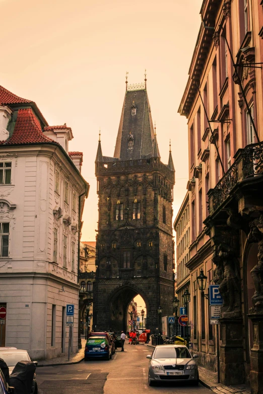 a group of cars driving down a street next to tall buildings, by karolis strautniekas, pexels contest winner, art nouveau, medieval gates, abandoned prague, at sunset, guillotine