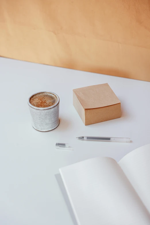 an open book sitting on top of a table next to a cup of coffee, a still life, trending on unsplash, postminimalism, cigarrette boxes at the table, pen on white paper, detailed product image, background image