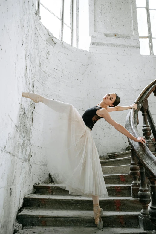 a woman that is standing on some stairs, by Elizabeth Polunin, trending on unsplash, arabesque, ballet style pose, silo, studio photo, half turned around