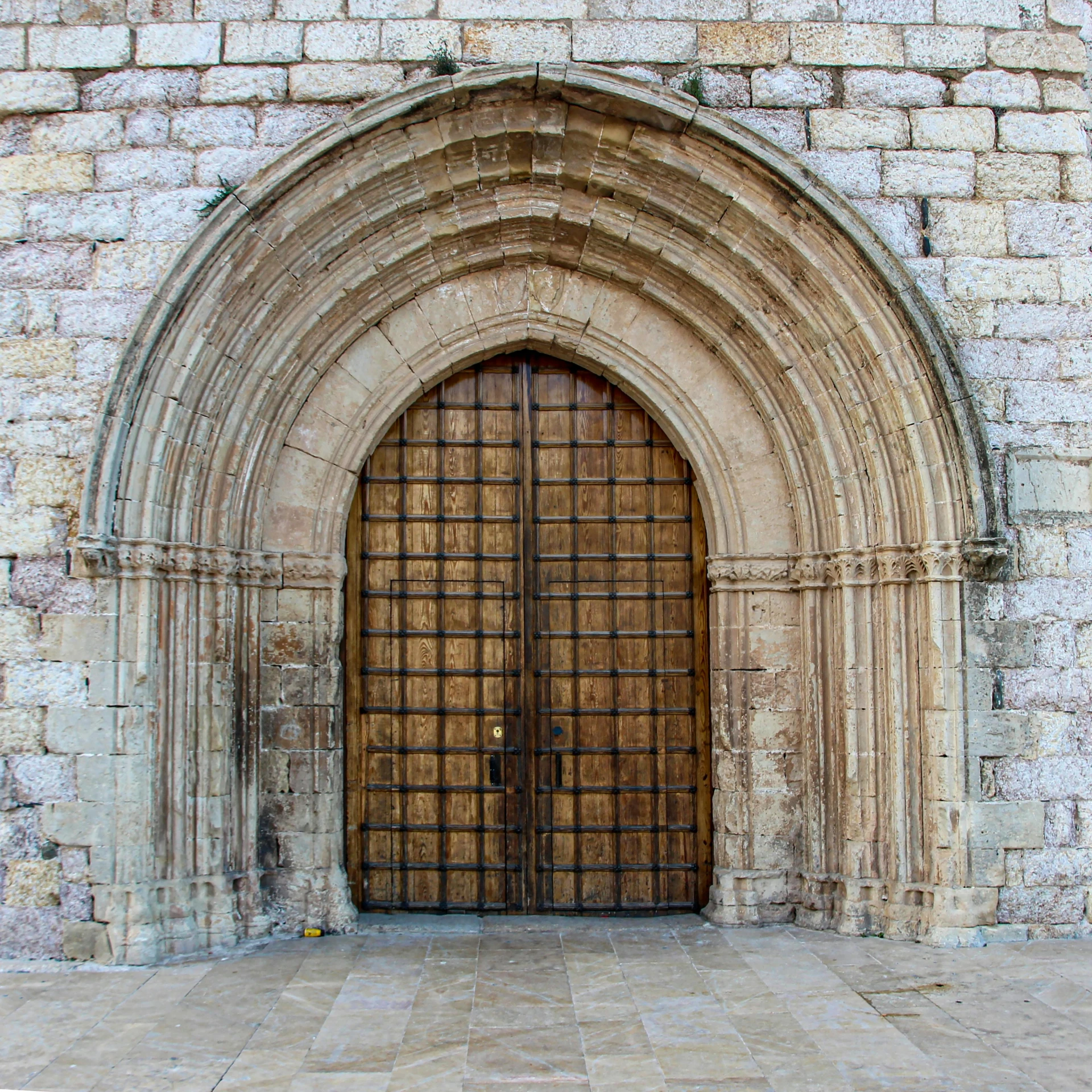 a large wooden door sitting inside of a stone building, an album cover, by Josep Rovira Soler, pexels contest winner, romanesque, square, archs, holy crusader medieval, where a large