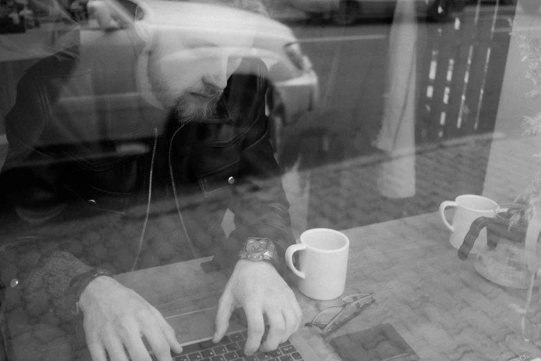 a man sitting at a table using a laptop computer, a photo, by Jan Rustem, small hipster coffee shop, reflections on a glass table, aphex twin, digital image