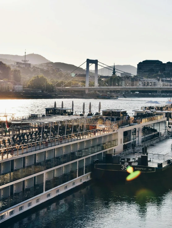 a river filled with lots of boats next to a bridge, on the deck of a ship, golden hour photograph, budapest, graphic”