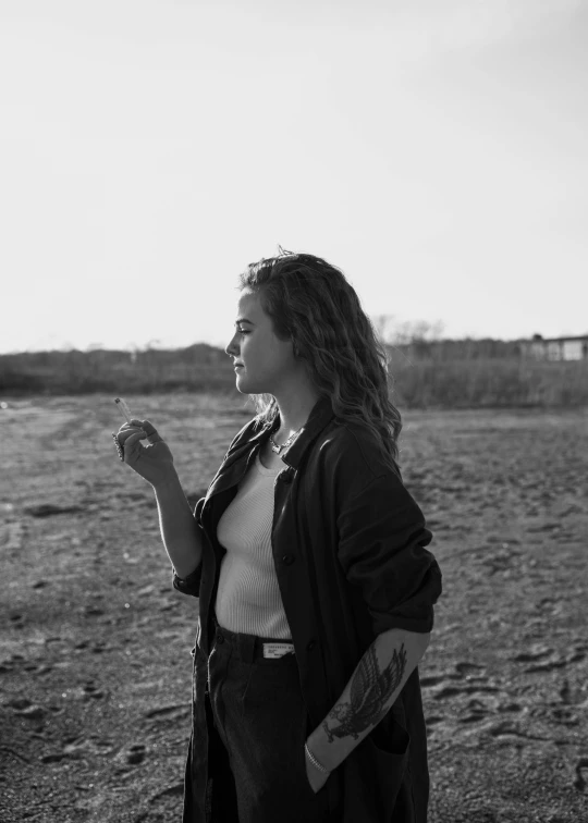 a black and white photo of a woman standing in a field, happening, holding a cigarette, profile image, beach, asher duran