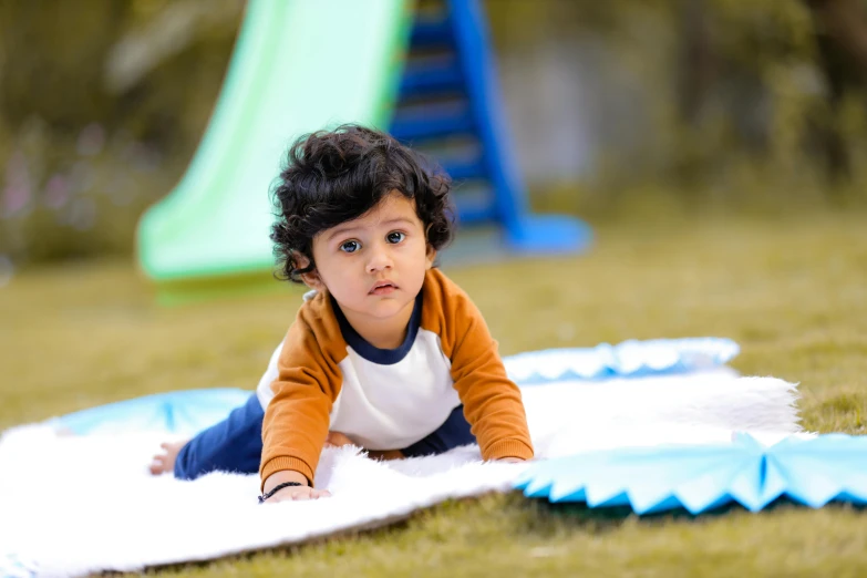 a small child laying on a blanket in the grass, by Lilia Alvarado, pexels contest winner, blue slide park, walking towards the camera, jayison devadas, activity play centre