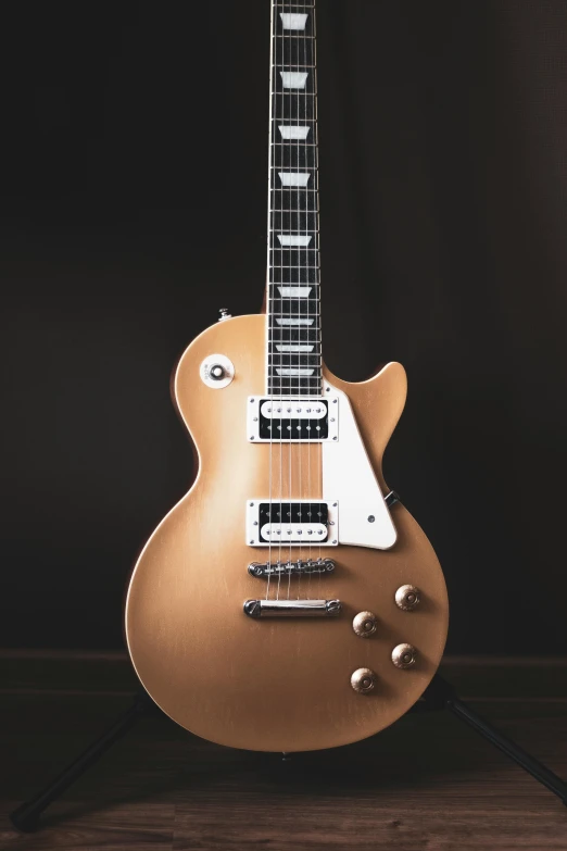a guitar sitting on top of a wooden floor, by Gavin Nolan, pexels contest winner, photorealism, brushed rose gold car paint, playing a gibson les paul guitar, shades of gold display naturally, replica model