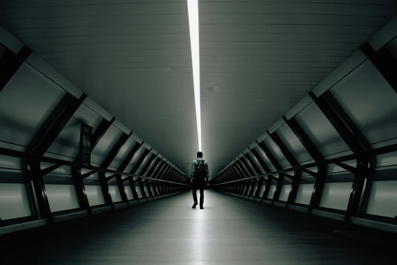 a person standing in the middle of a long hallway, a black and white photo, inspired by Beeple, unsplash contest winner, dark futuristic, symmetric lights, on a bridge, portrait featured on unsplash