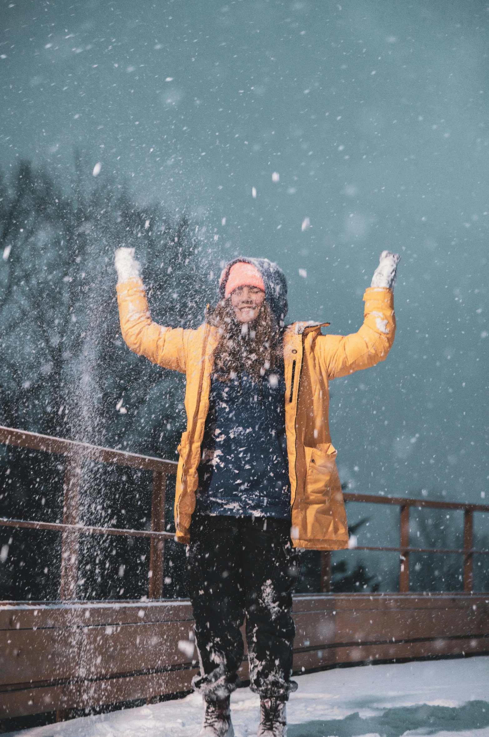 a man standing on a bridge in the snow, pexels contest winner, she expressing joy, wearing a yellow hoodie, snowflakes falling, hands in air