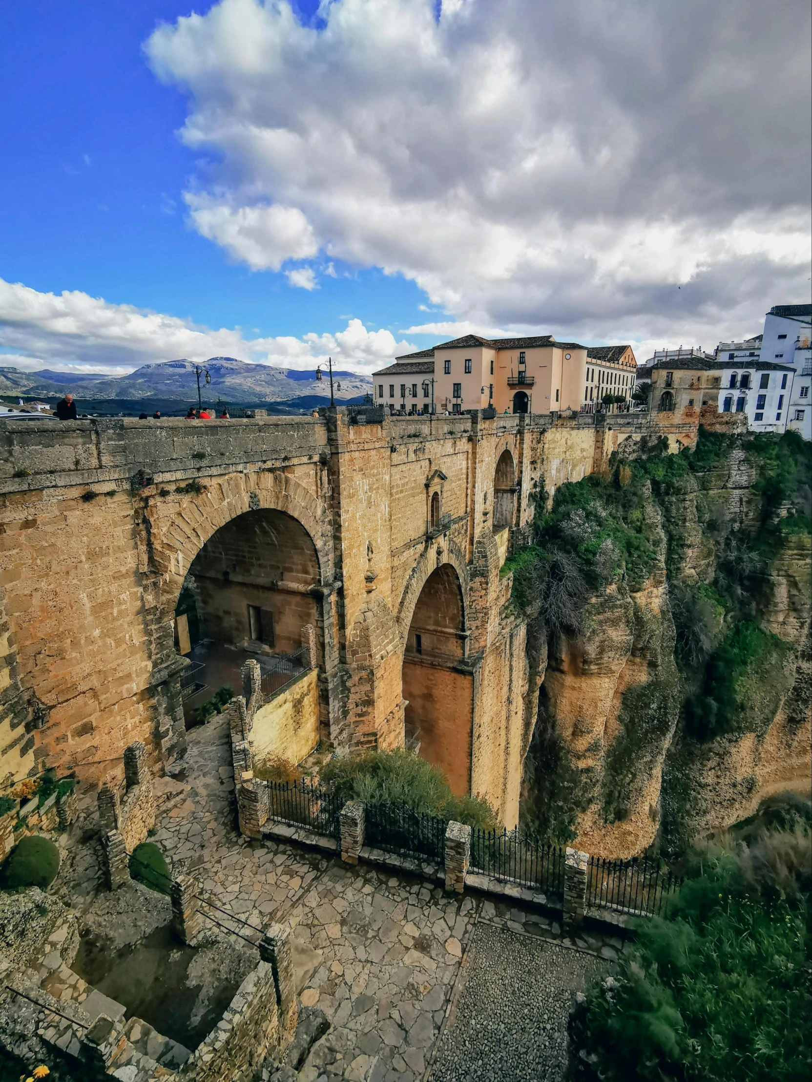 a group of people standing on top of a bridge, moorish architecture, 👰 🏇 ❌ 🍃, looking down a cliff, panoramic