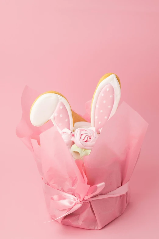 a cookie in a pink wrapper on a pink background, with bunny ears, detailed product image, pink rose, detail shot