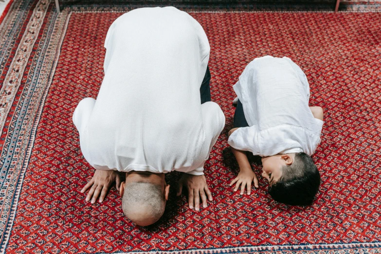 a couple of men standing on top of a rug, pexels contest winner, hurufiyya, praying posture, little boy wearing nun outfit, bent over posture, father with child