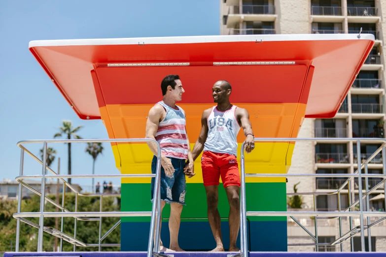 a couple of men standing on top of a boat, by Carey Morris, pride month, in a beachfront environment, fourth of july, colorful uniforms