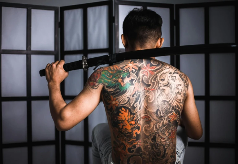 a man with a tattoo on his back holding a sword, a tattoo, inspired by Kanō Hōgai, pexels contest winner, studio photo, ross tan, over the shoulder, full color