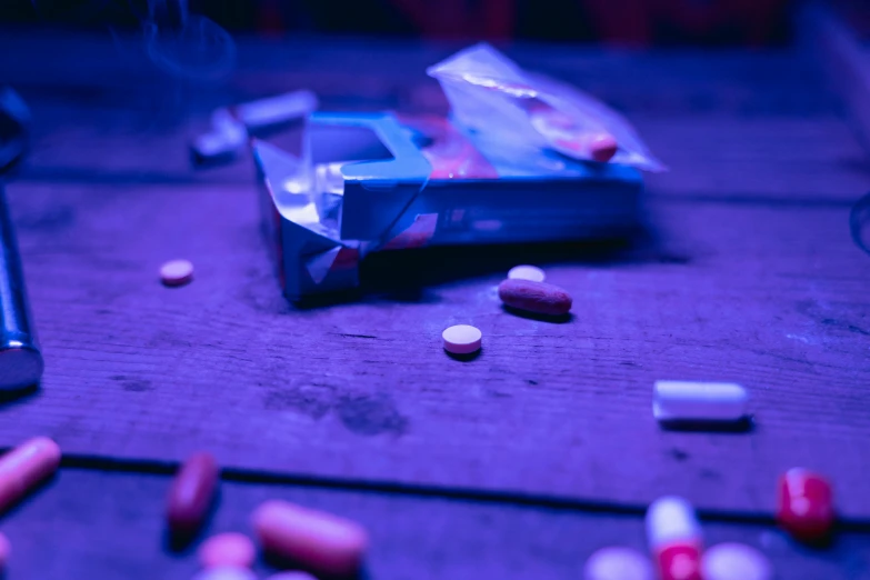 a bunch of pills on a table next to a cell phone, by Sebastian Vrancx, unsplash, antipodeans, purple and blue neon, still from the movie 8 mile, a wooden, blood collection vials