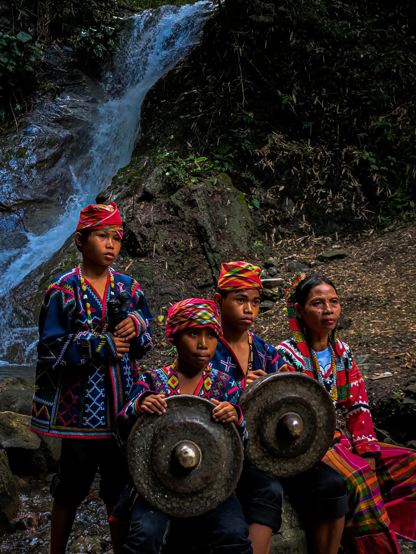 a group of people standing in front of a waterfall, an album cover, by Jan Verkolje, pexels contest winner, sumatraism, tribal armor, bells, philippines, wearing traditional garb