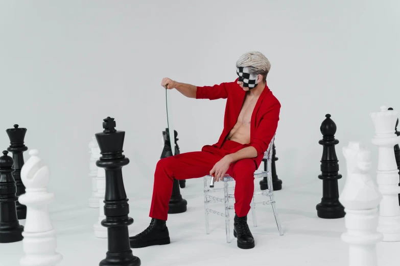 a man sitting on a chair surrounded by chess pieces, an album cover, pexels contest winner, aestheticism, red jumpsuit, white man with black fabric mask, 2019 trending photo, xqc