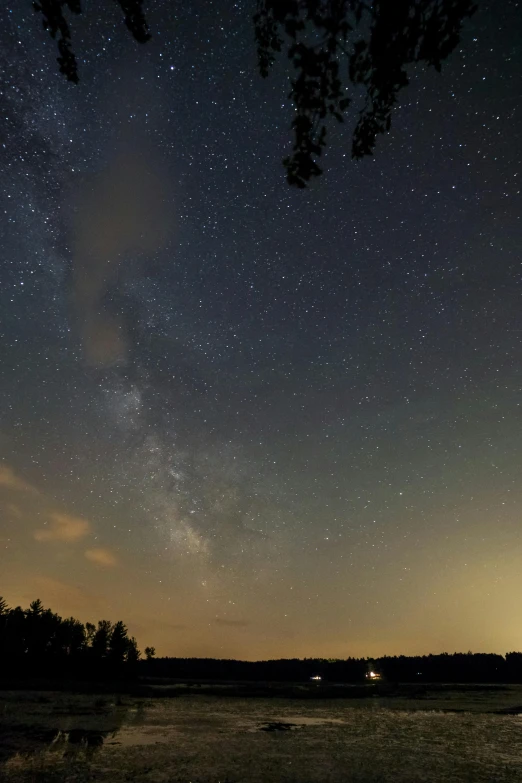 a large body of water under a night sky, over the tree tops, the milk way up above, skyline showing, dust partiles in the air