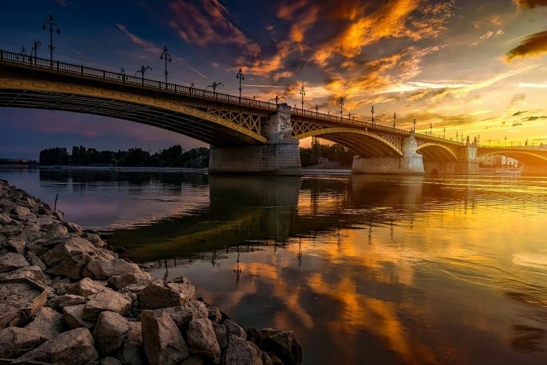 a bridge over a body of water at sunset, by Gabor Szikszai, pexels contest winner, budapest, shades of gold display naturally, river of wine, detailed photo 8 k