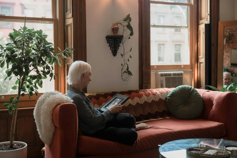 a woman sitting on a couch reading a book, by Harriet Zeitlin, pexels contest winner, white haired, old apartment, profile image, took on ipad