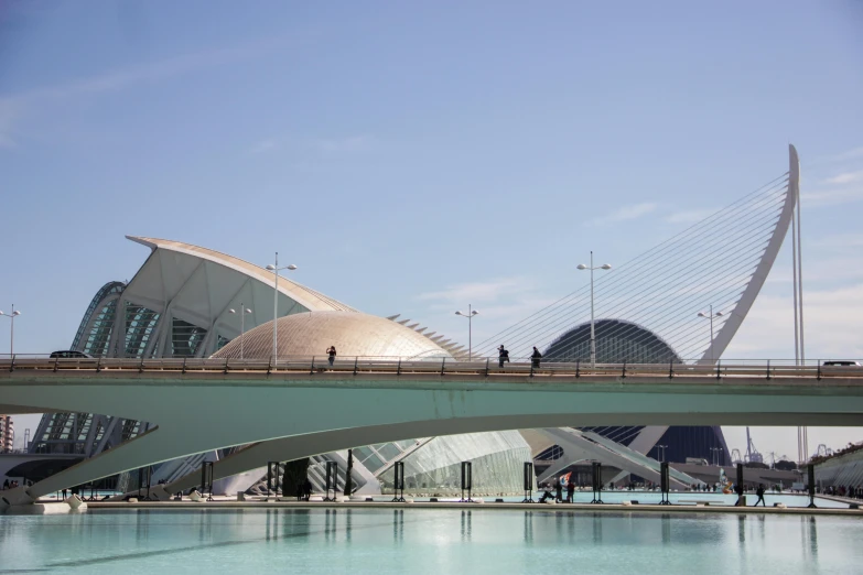 a bridge over a body of water with a building in the background, inspired by Pedro Álvarez Castelló, pexels contest winner, modernism, futuristic dome, calatrava, people walking around, costa blanca