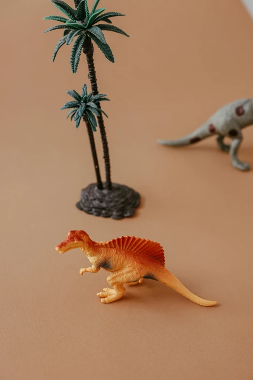 a couple of toy dinosaurs sitting on top of a table, inspired by Adam Rex, trending on unsplash, a palm tree, brown resin, detailed product image, detail shot